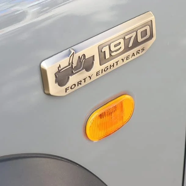 Close-up of a vintage vehicle badge reading '1970 Forty Eight Years' with an illustration of a vintage vehicle and an orange side marker light.