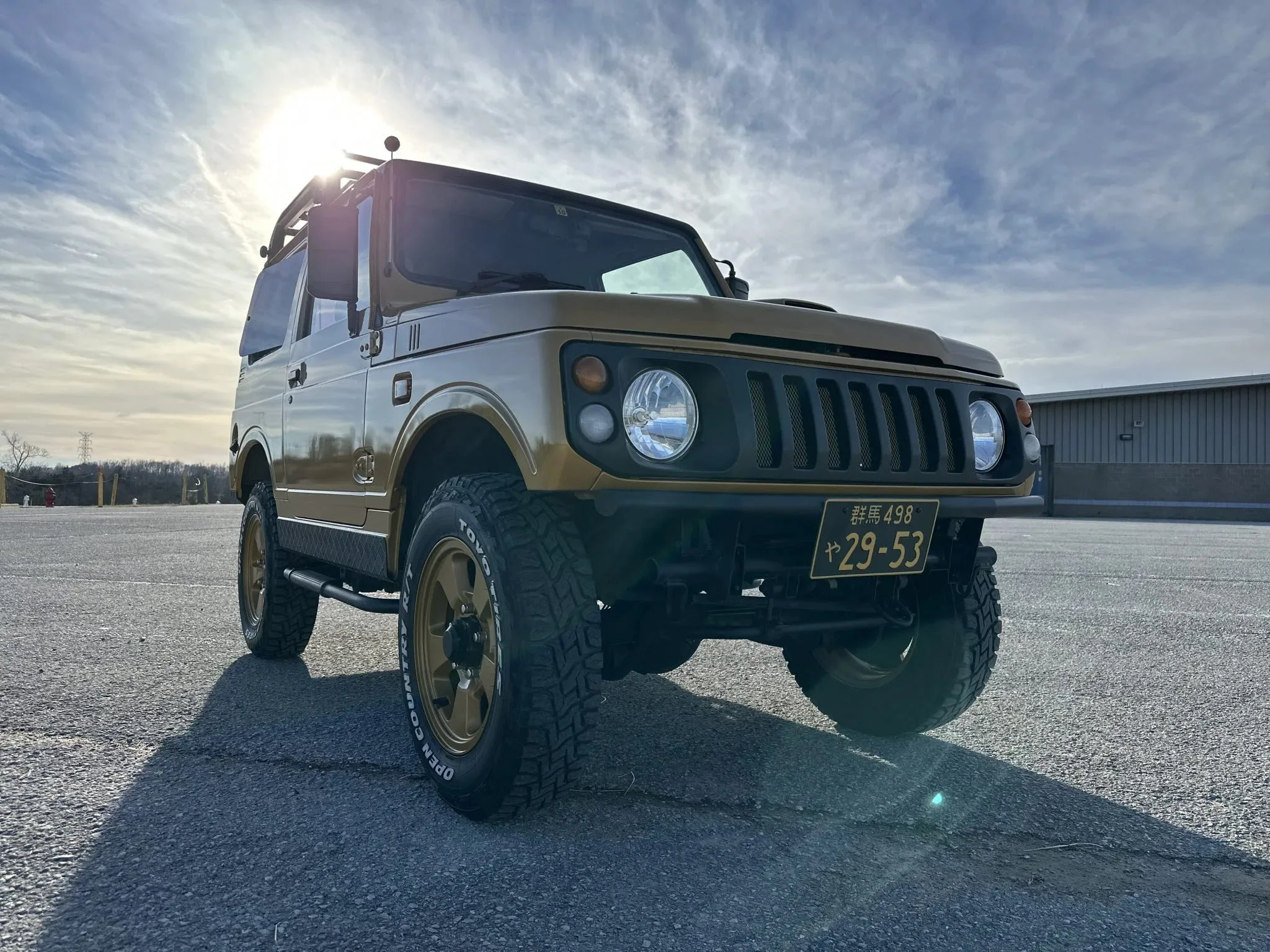 Off-road vehicle with Japanese license plate, parked on concrete under a cloudy sky.