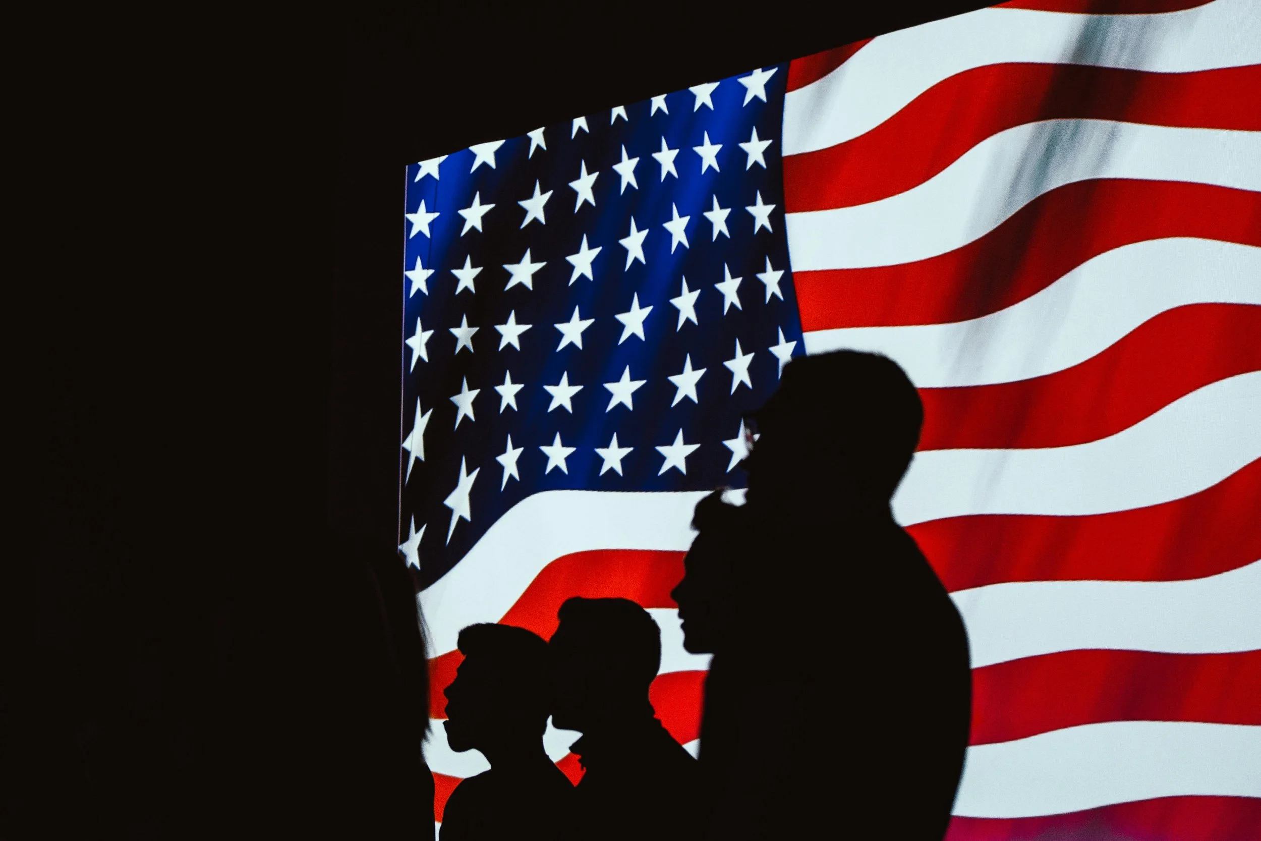 Silhouettes of people in front of a large American flag.