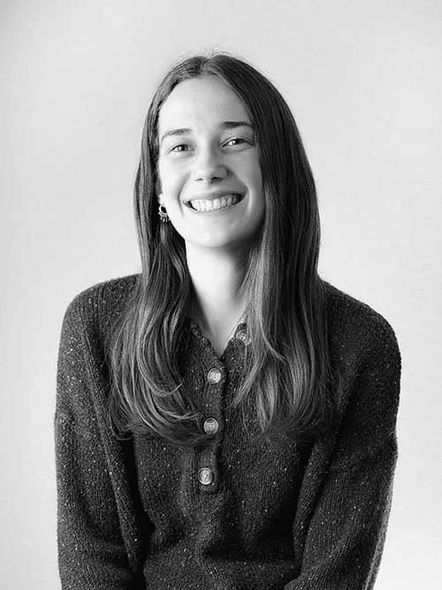 A young woman with curly brown hair and a white t-shirt smiling at a table in a restaurant.