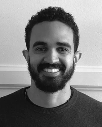 Portrait of a smiling man with curly hair and a beard, in black and white.
