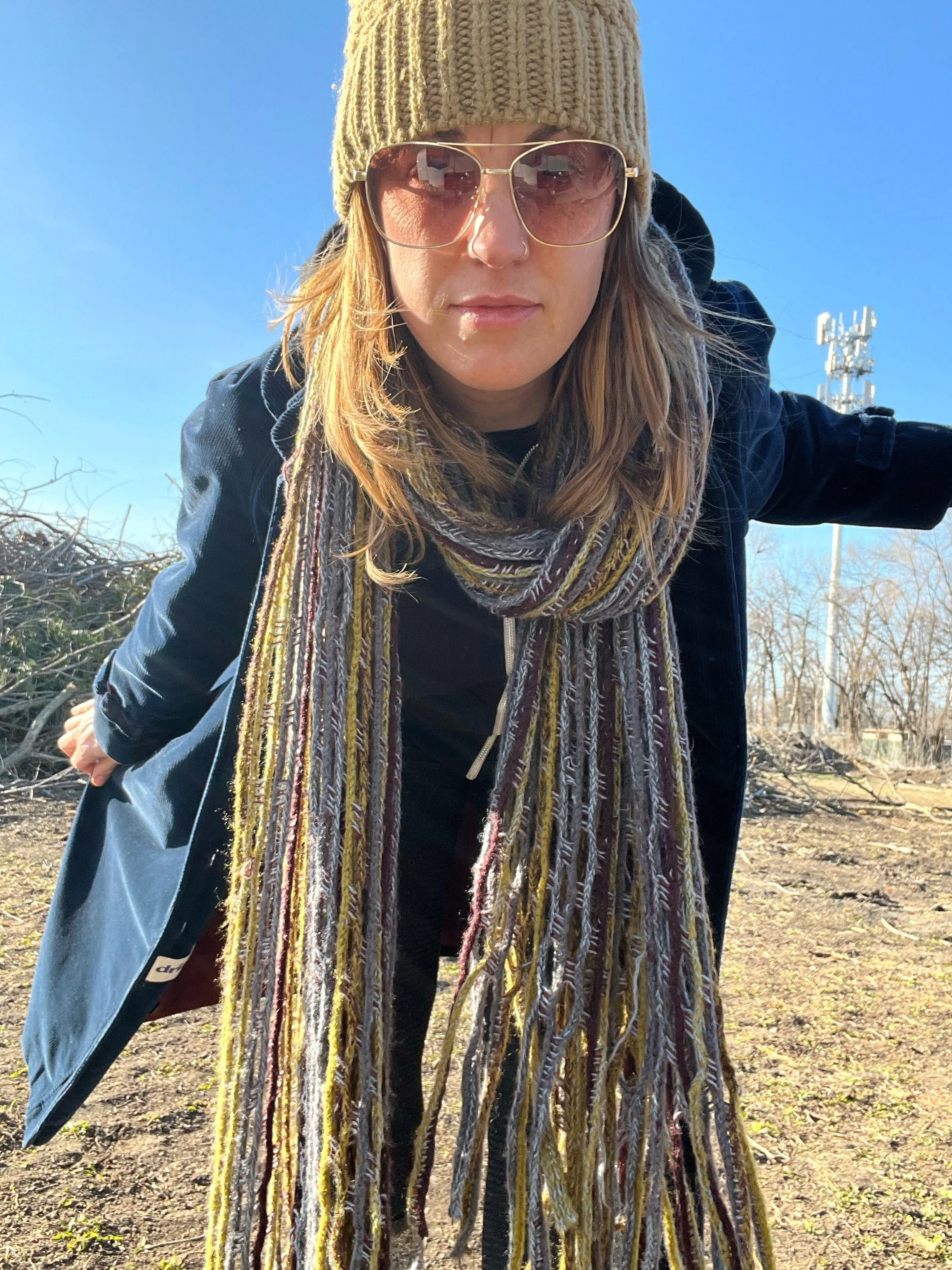 Person wearing a knit hat, sunglasses, and a long scarf outdoors in clear weather