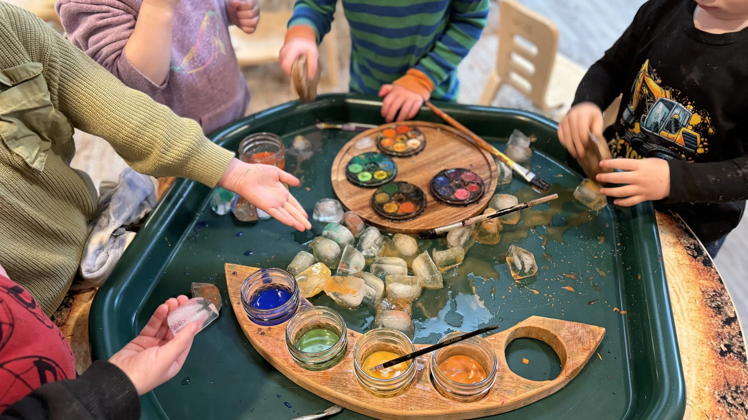 Children gathered around a water table with ice and colorful paints, engaging in sensory play.