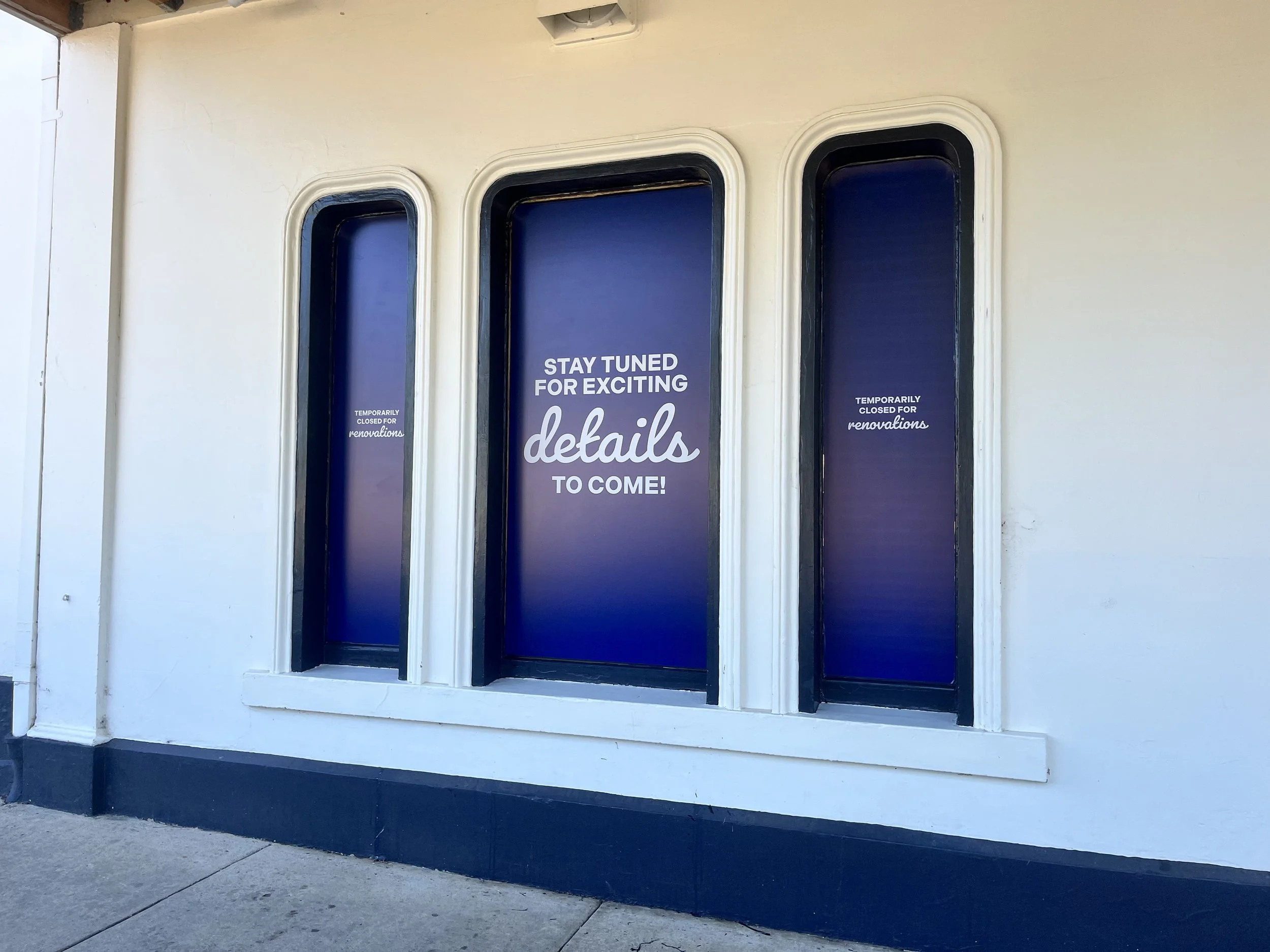 Building windows with purple posters that say, 'Stay tuned for exciting details to come!' and 'Temporarily closed for renovations.'