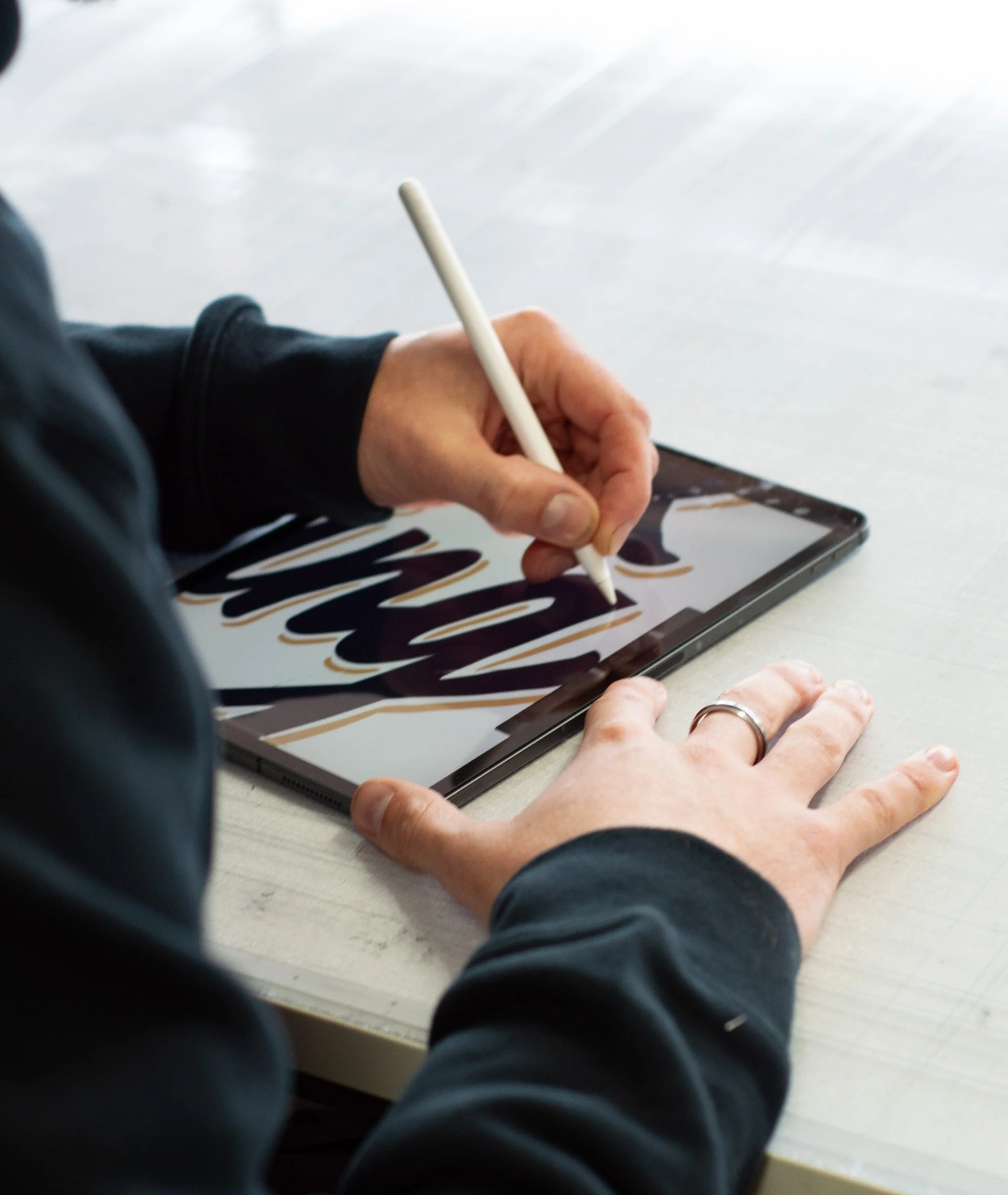 Person using a stylus on a tablet to create digital art with bold black and brown strokes.