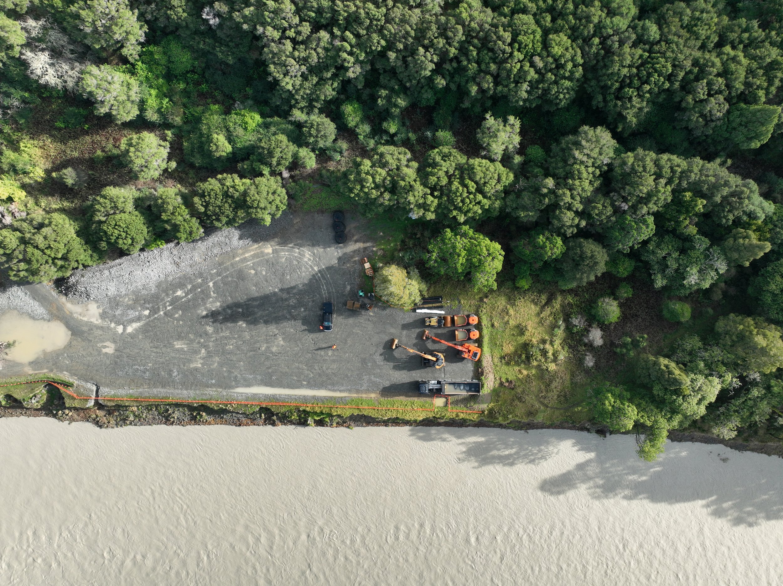 Two large excavators creating a retaining wall beside a coastline