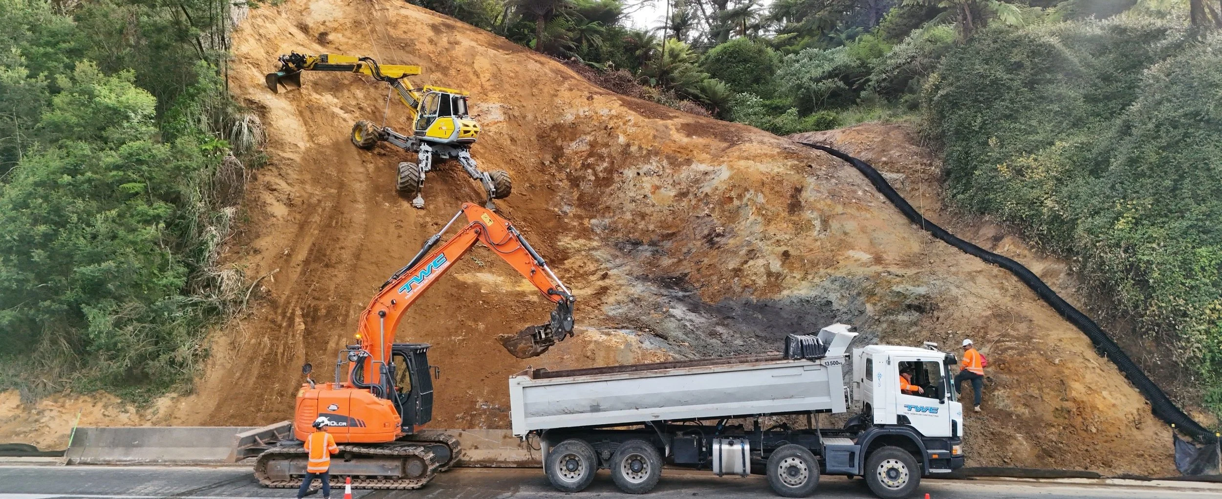Two large excavators creating a retaining wall beside a coastline