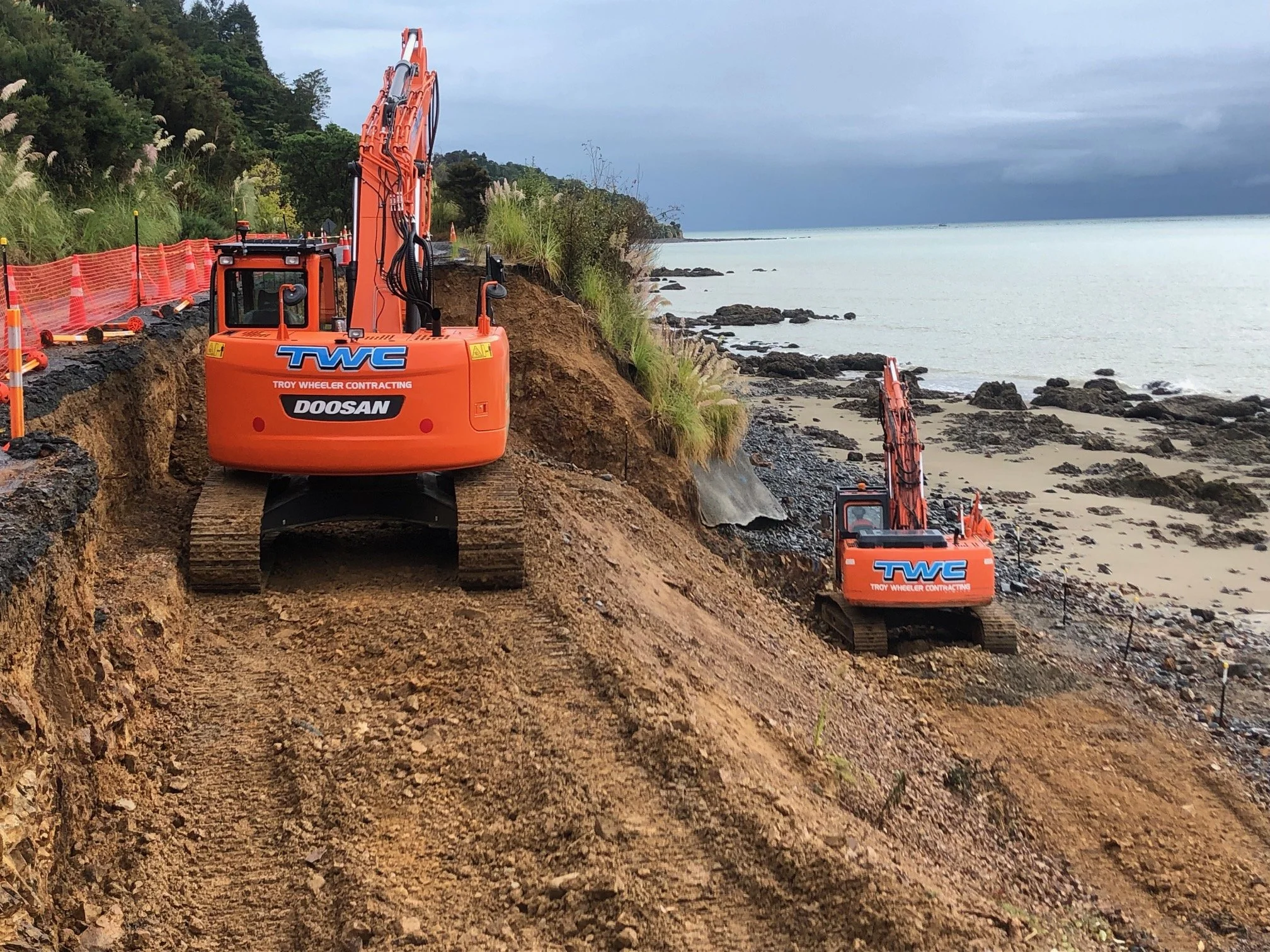 Two large excavators creating a retaining wall beside a coastline