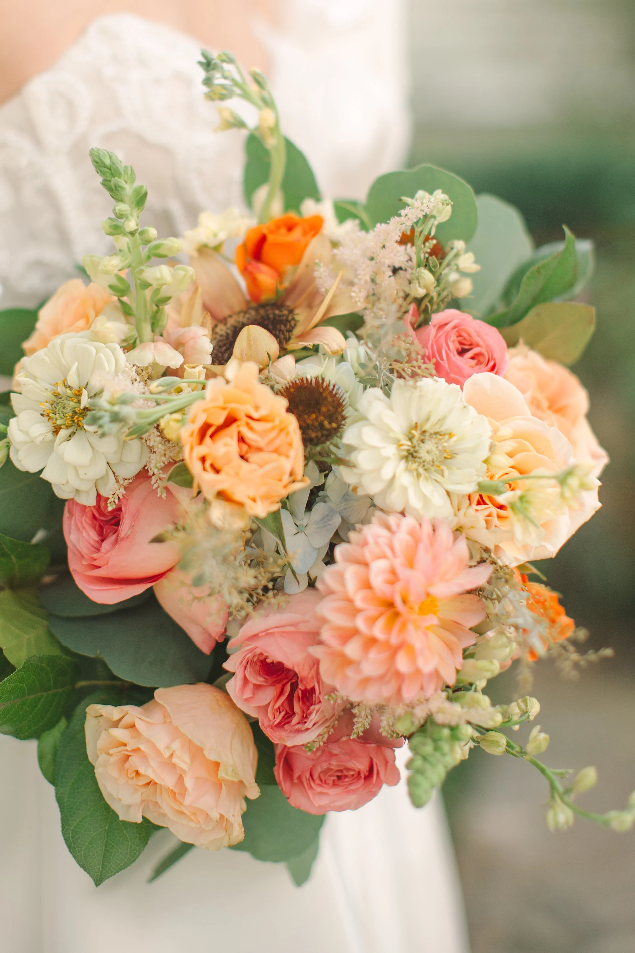 Close-up view of a bouquet of assorted flowers with pink, peach, white, and orange blooms.