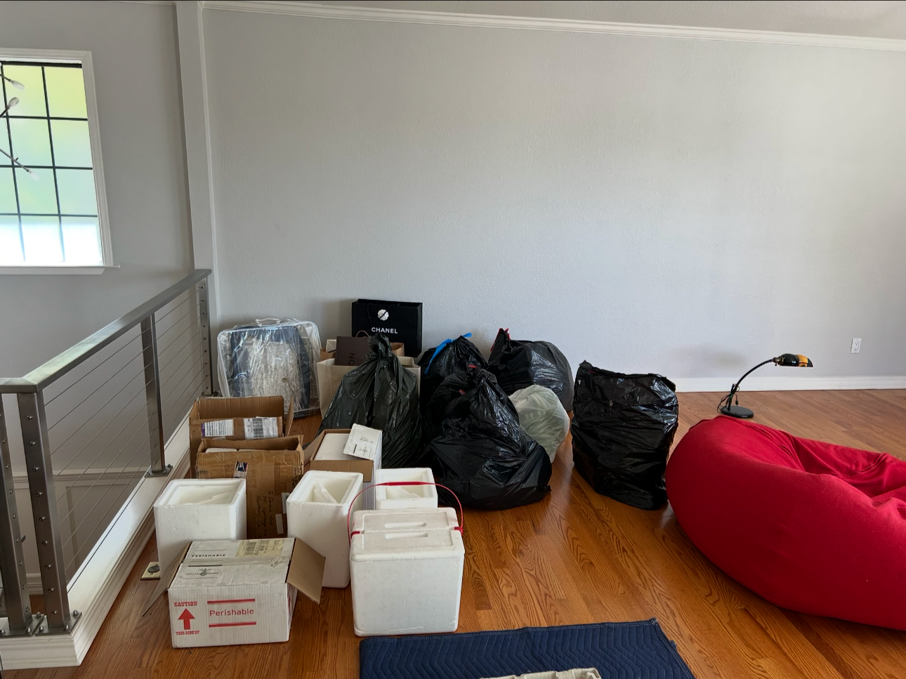 Empty room with various bags and boxes, a red chair, and a lamp on the floor.