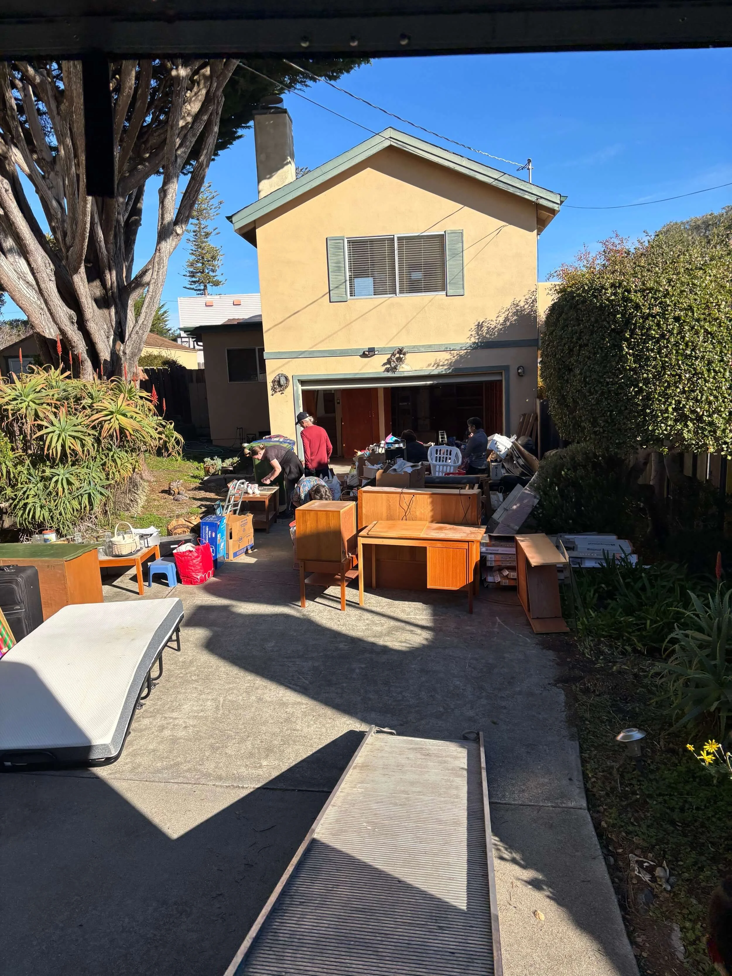 People sorting through items in the driveway of a house during a yard sale on a sunny day with blue sky. monterey junk removal.