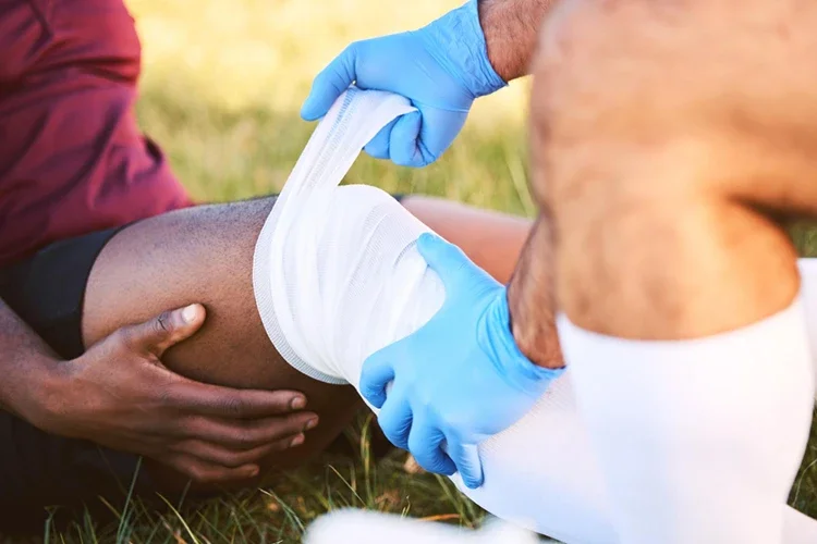 An athlete receiving medical attention for a knee injury on the field, with a medic applying a bandage for pain relief and stabilization.