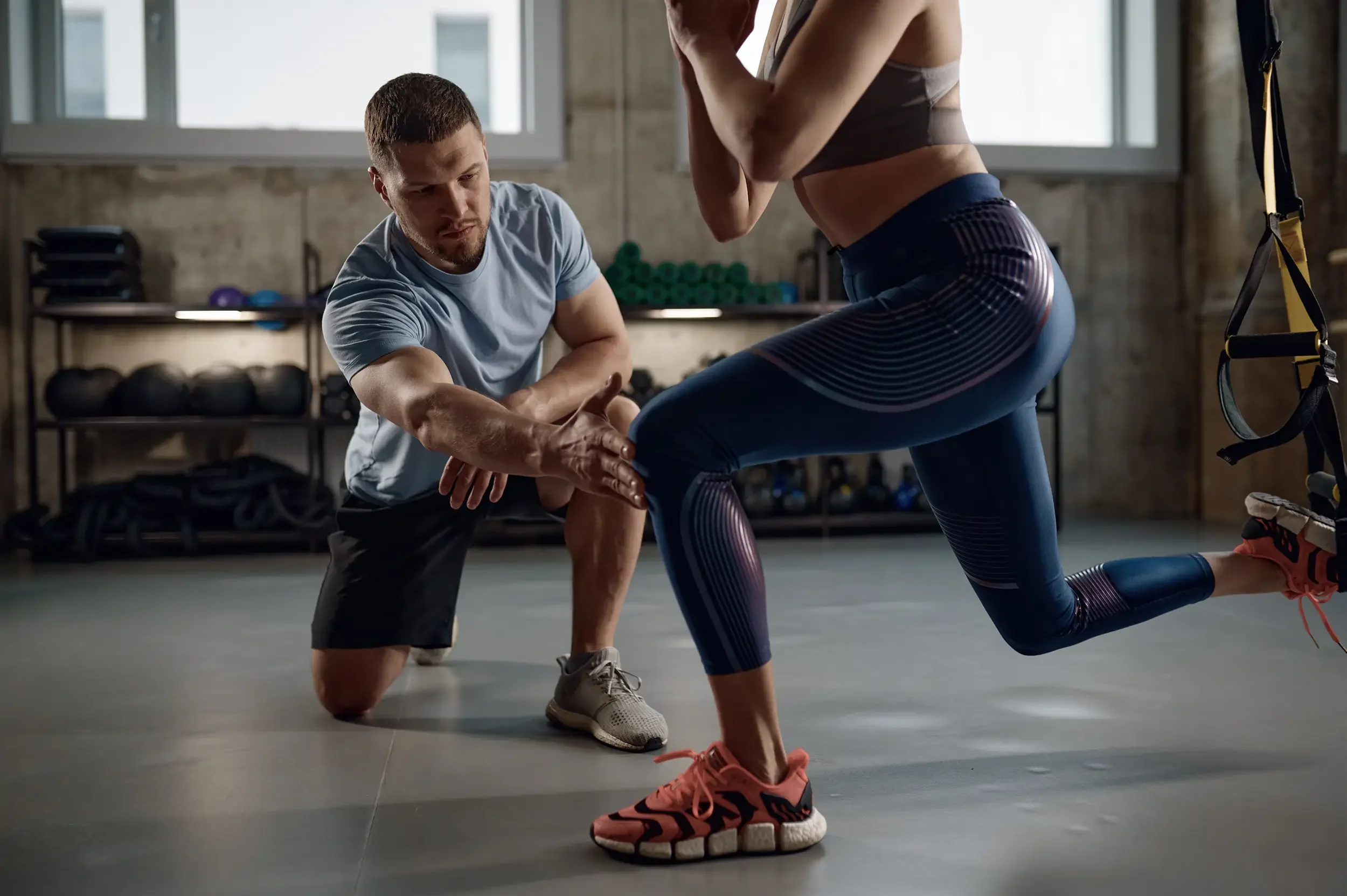 A young athletic woman performing leg training with suspension straps under the supervision of a chiropractor to ensure proper form and balance.