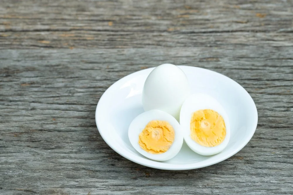 Boiled eggs on a white ceramic plate placed on a wooden table — a protein-rich, low-carb snack perfect for healthy diets and meal prep.