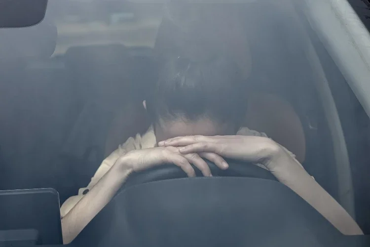 A woman in the driver’s seat resting her head on the steering wheel with an upset expression, struggling with anxiety after a crash.