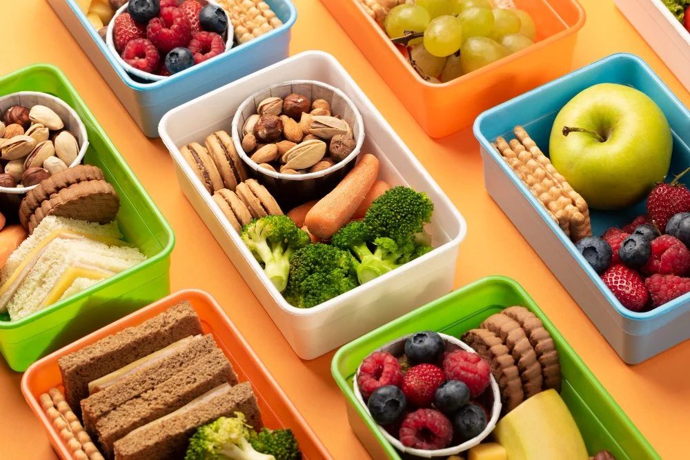 High-angle view of healthy snack boxes filled with fresh fruits, vegetables, nuts, cheese, and whole-grain snacks — a balanced, nutrient-dense option for clean eating on the go.