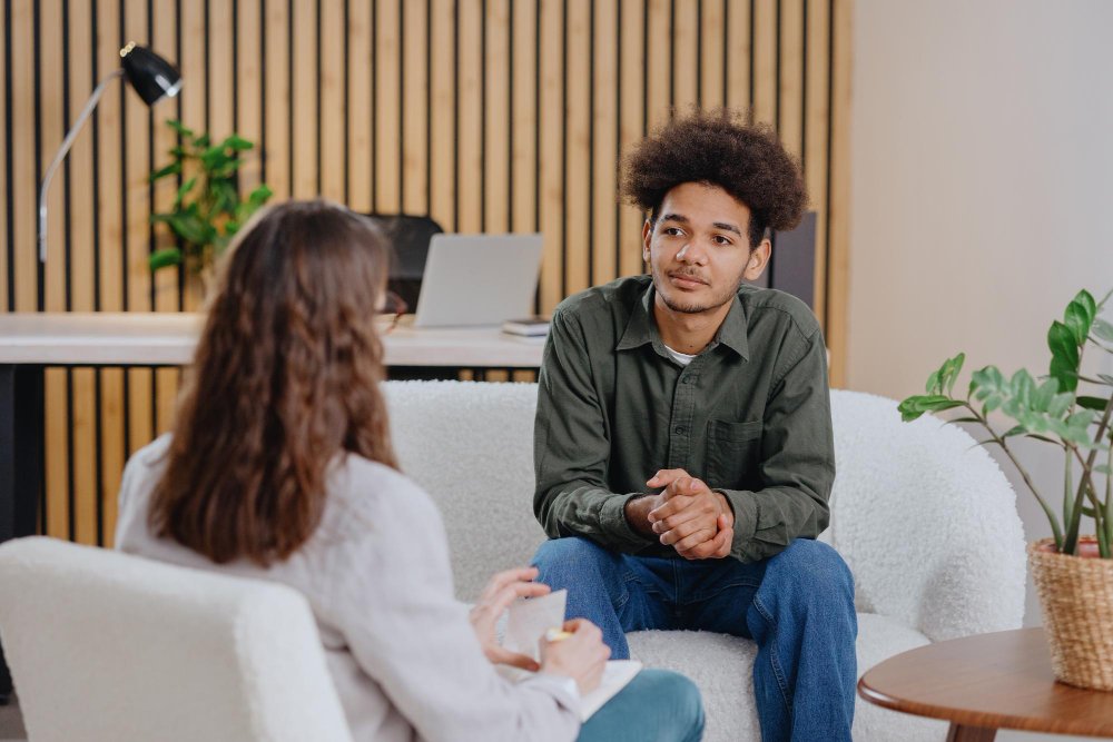A young man sitting across from a female therapist during a counseling session, expressing emotions in a safe and supportive environment.