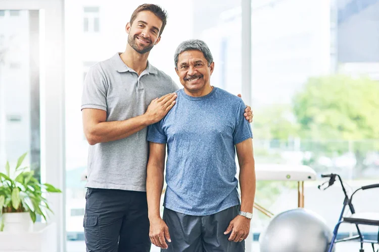 A portrait of a young male physiotherapist and an elderly male patient smiling together.