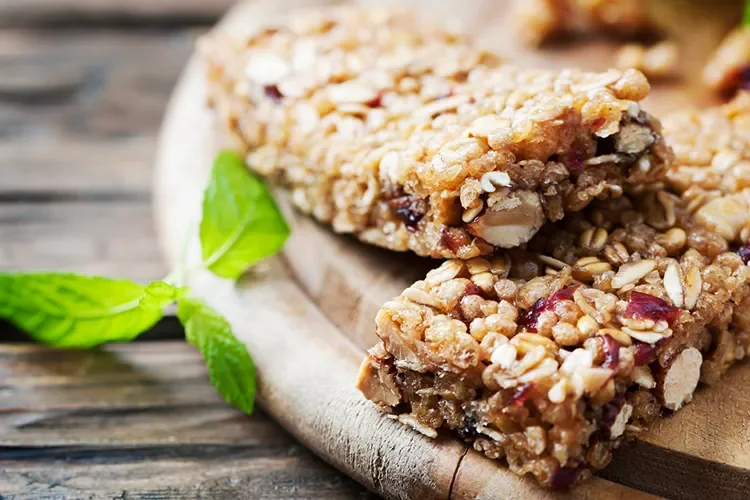 Two crunchy energy bars made with wholesome ingredients like nuts, seeds, and oats are presented on a wooden board with a sprig of mint. These low-sugar bars provide sustained energy without a sugar crash, making them perfect for busy days.