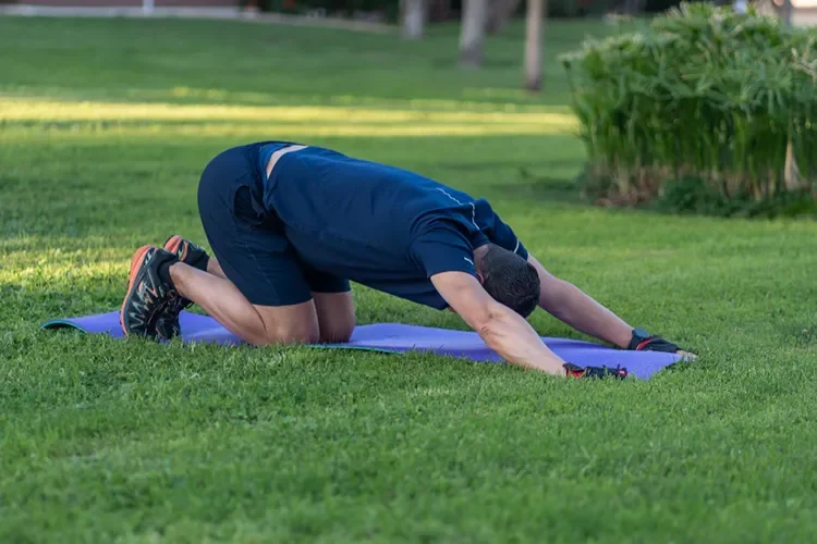 A person performing a child’s pose stretch outdoors to improve flexibility, support spinal health, and maintain proper alignment at home.