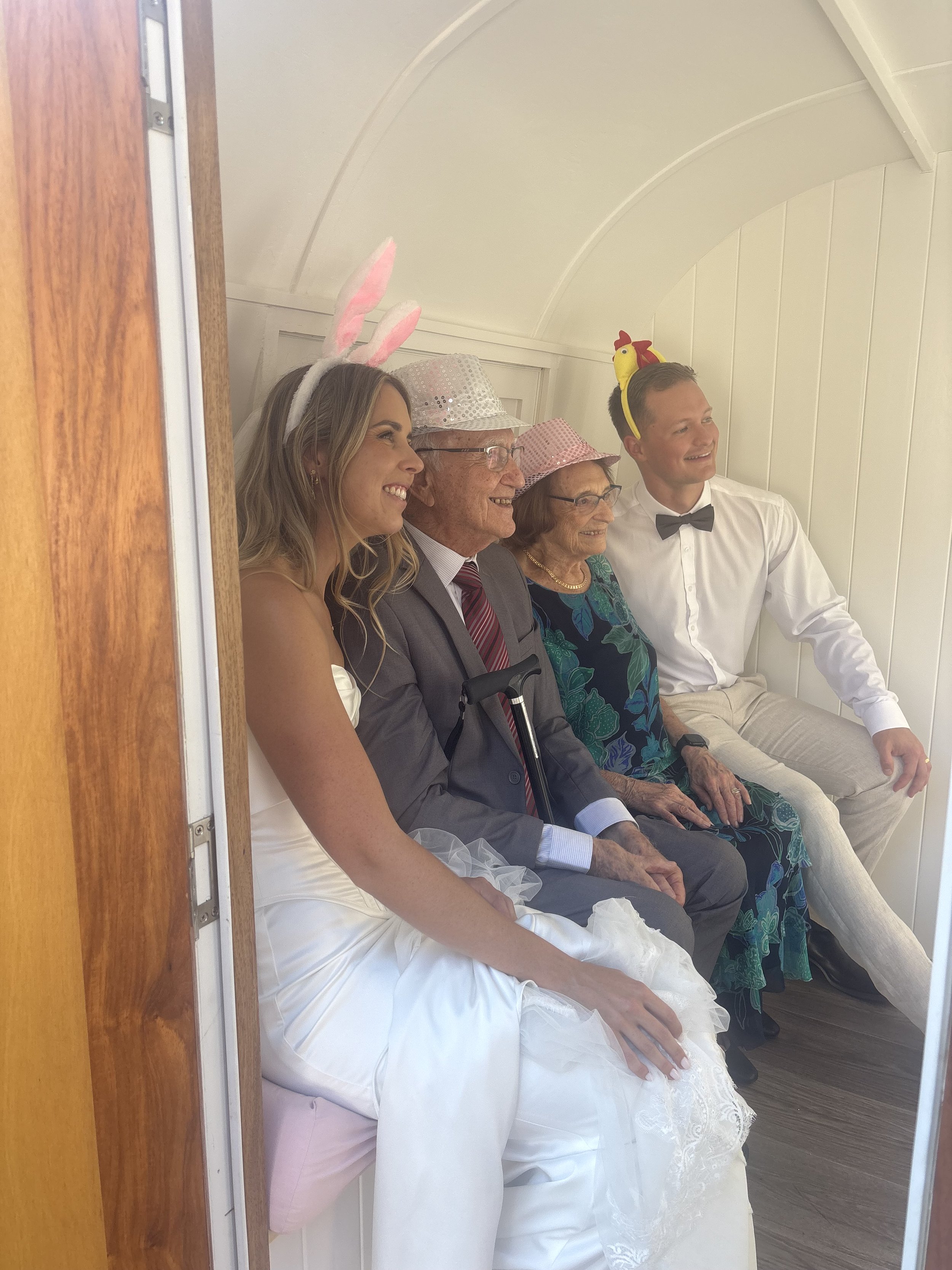 Five people sitting on a white bench in a small, white, curved room, dressed in festive costumes for a celebration or holiday.
