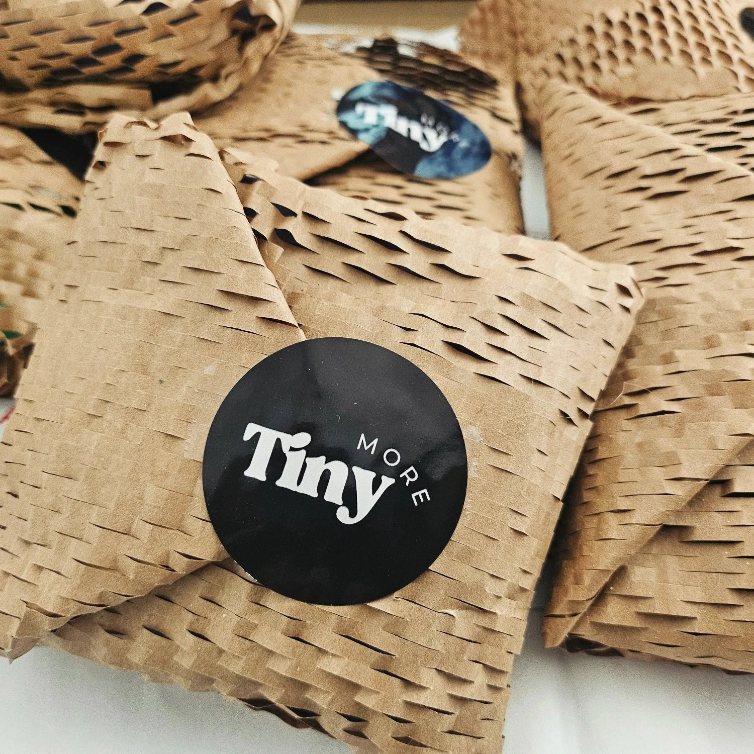 Tiny More packaging of items in brown paper covers using Australia Post for tracked delivery. Tiny More logo prominent in image.
