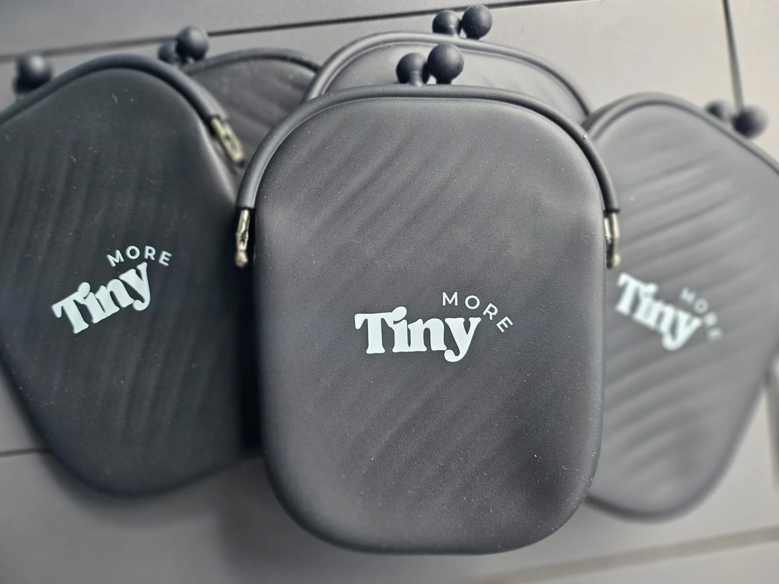 Close-up of three small black cases with zippers, each bearing the phrase "Tiny More" in white across the front. Showing quality silicone material that is splash-proof and can be re-purposed.