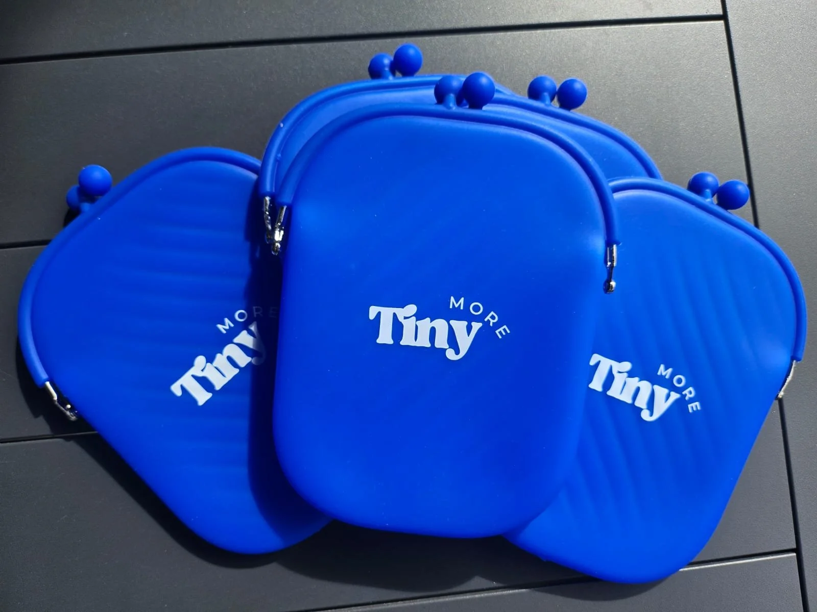 Three blue miniature containers with the words "Tiny More" printed on them in white text. Showing quality silicone material that is splash-proof and can be re-purposed.
