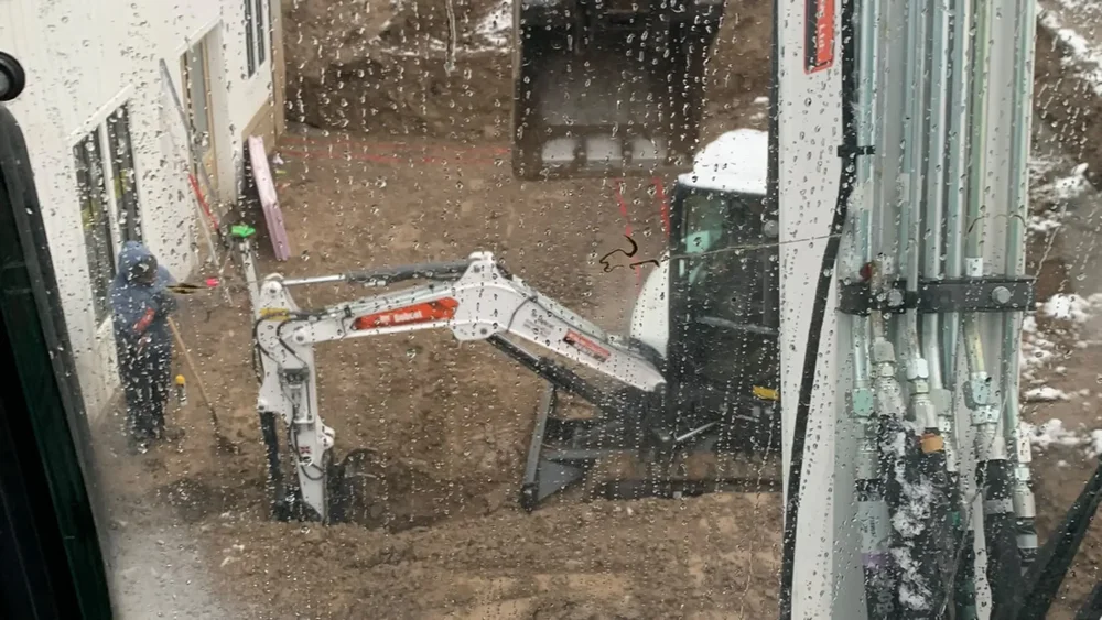 excavator digging a basement walkout cut beside a home