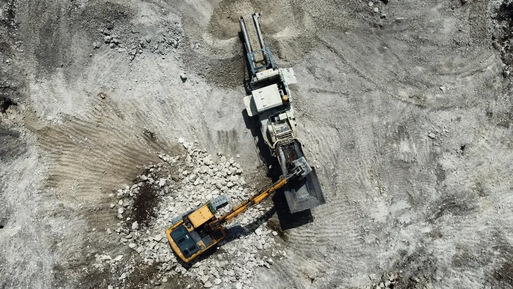 Excavator feeding broken concrete into a mobile crusher for removal and recycling