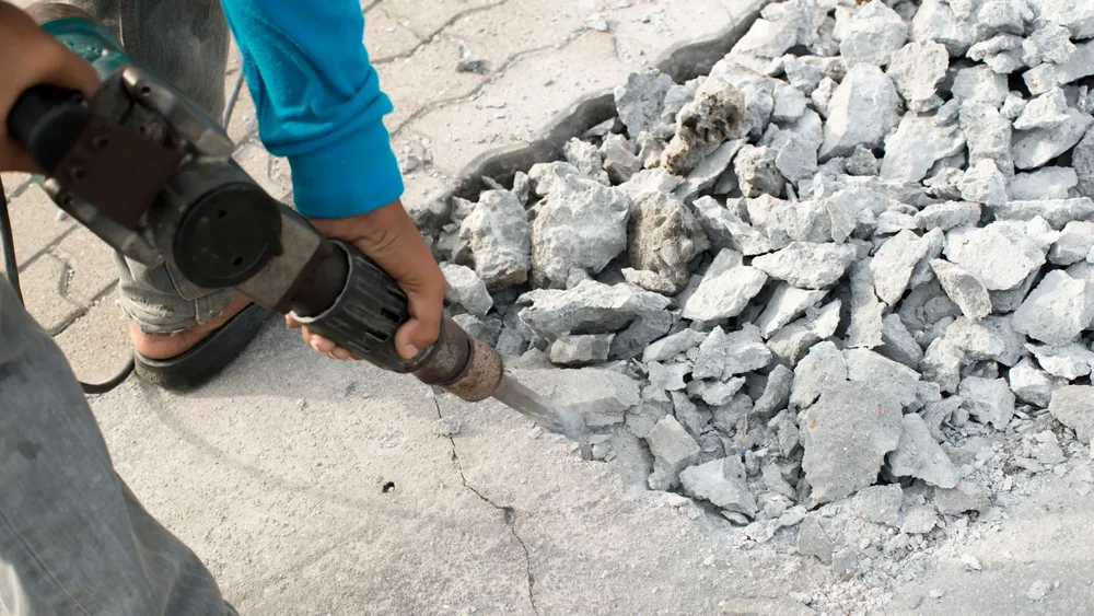 Worker jackhammering concrete into rubble during professional removal