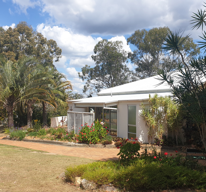 A modern white house with a garden, surrounded by trees, under a partly cloudy sky.
