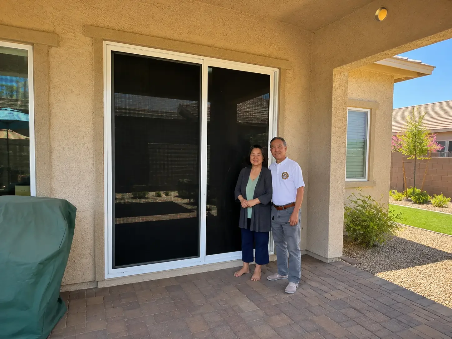 Santa Clarita homeowners stand beside a dark security screen on their patio door, showing a protective option that keeps the home’s exterior HOA-friendly.