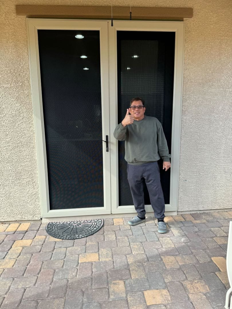 A man standing in his home's entryway, giving a thumbs-up next to a new black and white security screen door.