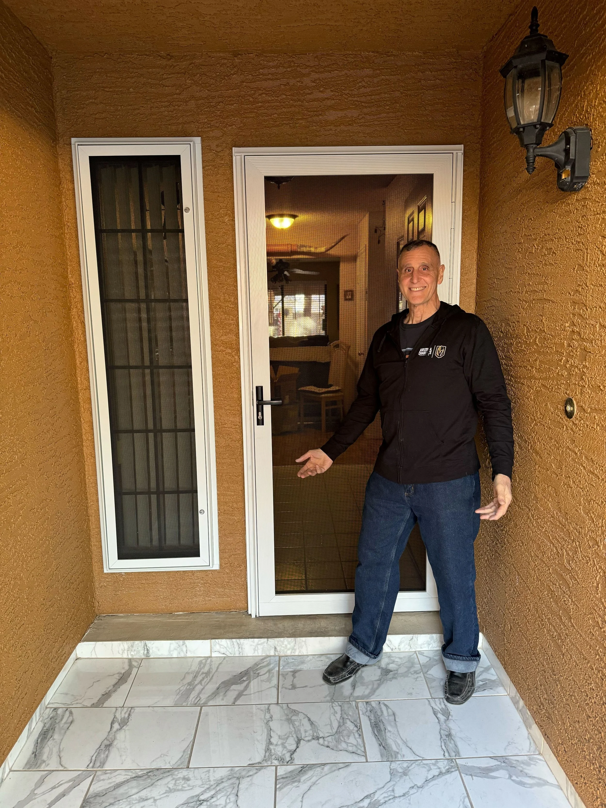 A man stands smiling in a tiled entryway next to a white-framed security screen door he just had installed.