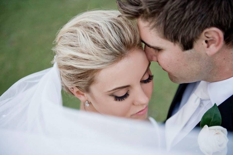 Close-up of a bride and groom touching foreheads with eyes closed, on their wedding day, outdoors.
