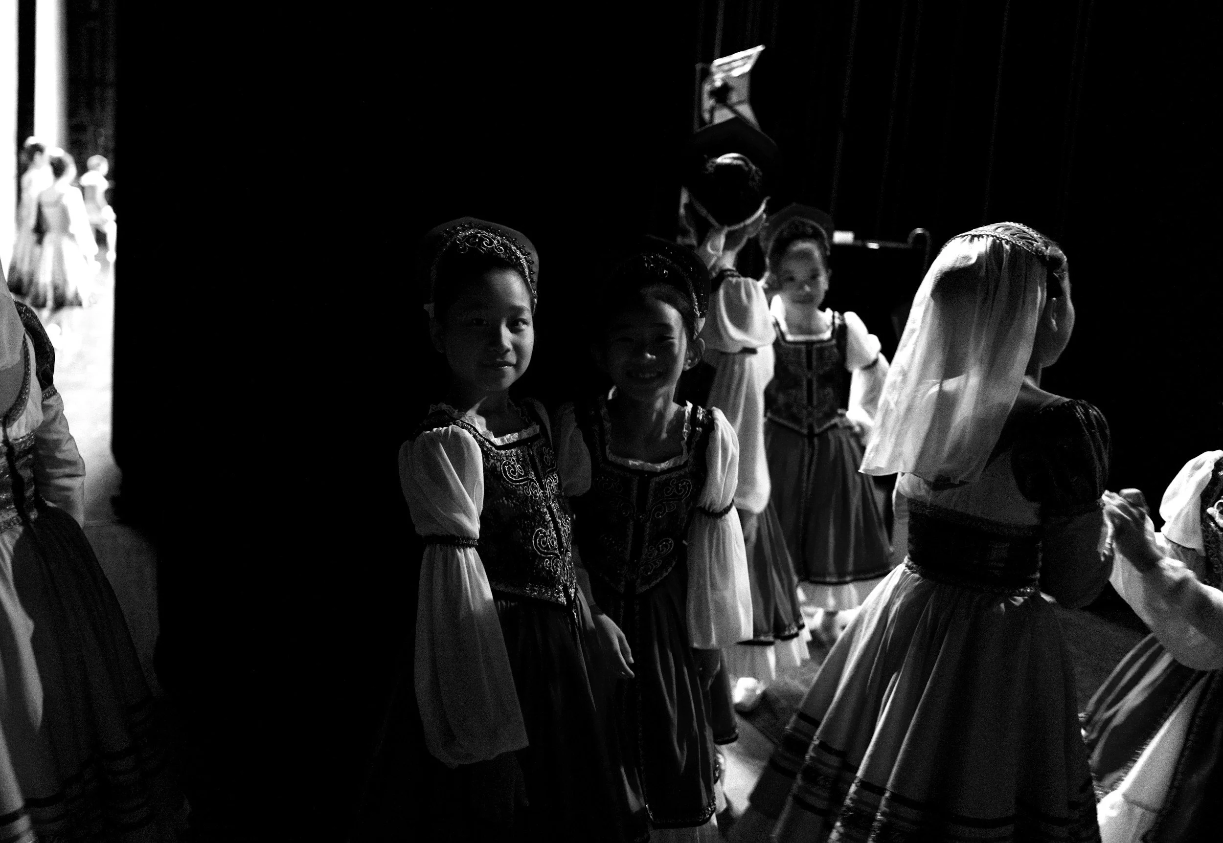 Children dressed in traditional folk costumes, standing in line backstage, preparing for a performance.