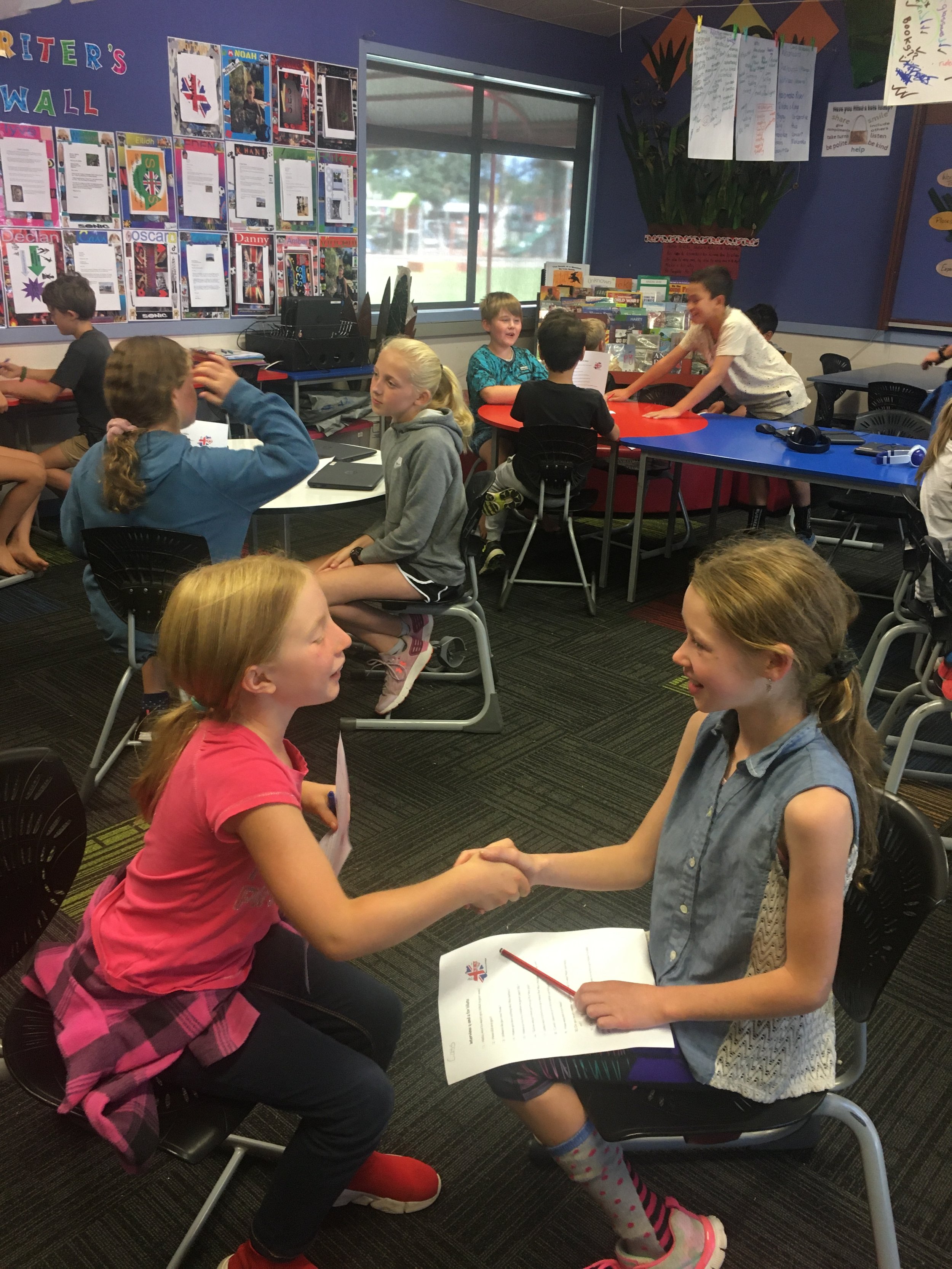 Two girls are shaking hands and exchanging papers in a classroom. Interviewing each other during a Mantle