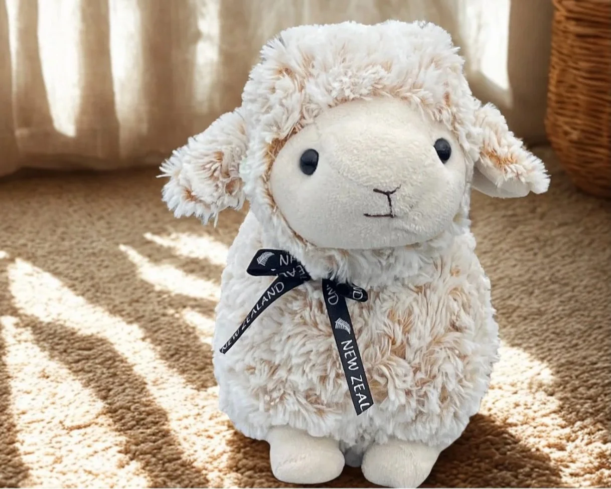 Plush toy representing a sheep with a bow with New Zealand engraved on it