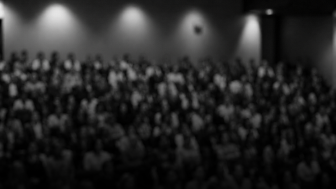 Black and white photo of a large audience seated in a theater or auditorium, facing the stage.