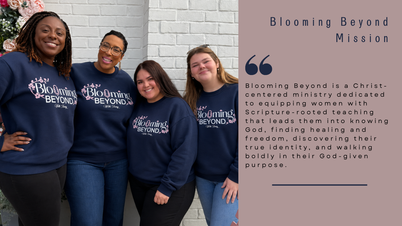 Four women wearing matching Dark blue sweatshirts with 'Blooming Beyond' logo, standing close to each other, smiling, in front of a white brick wall and some pink flowers.