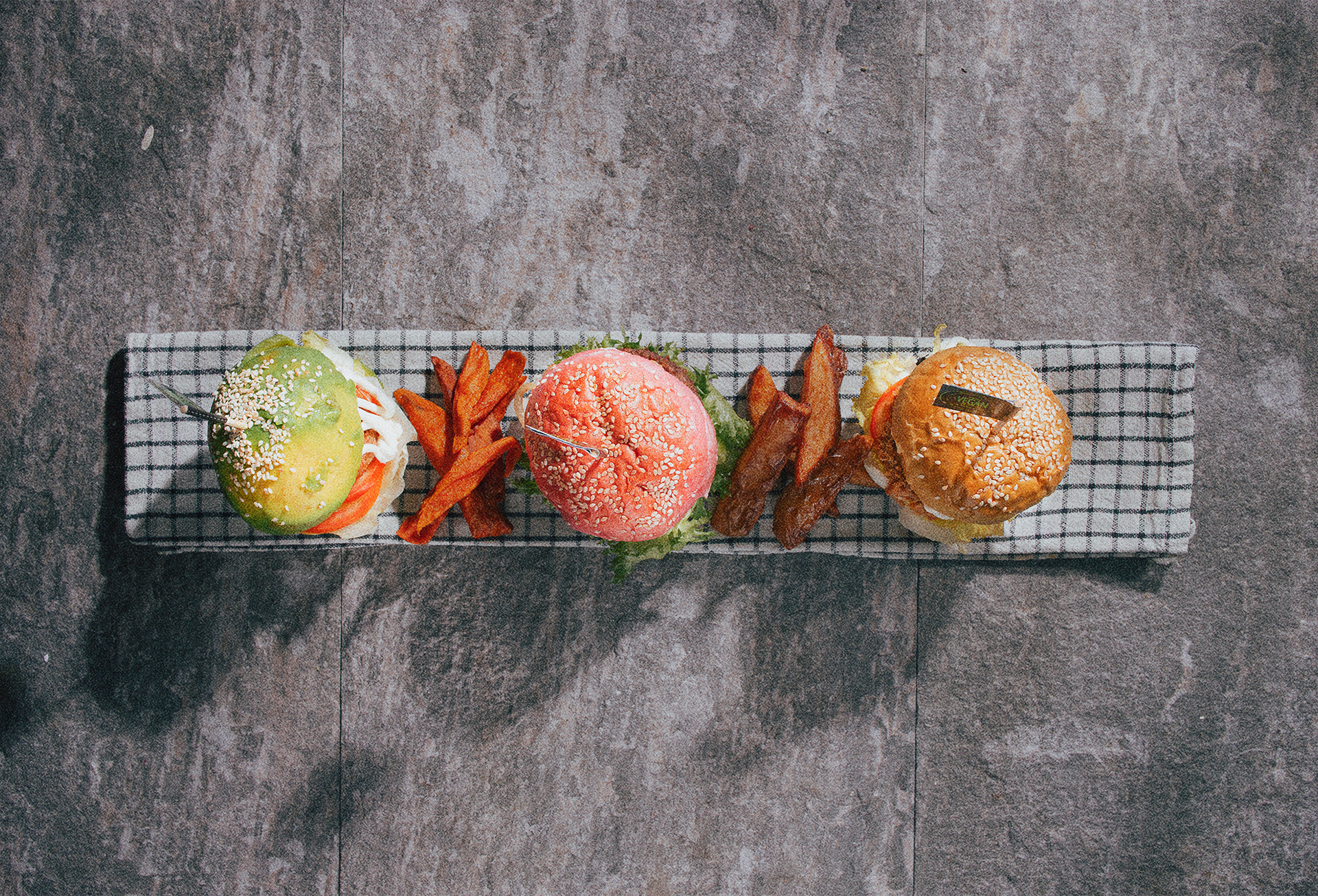 Top view of three vegan sliders with sweet potato fries on a rectangular checkered plate on a wooden surface