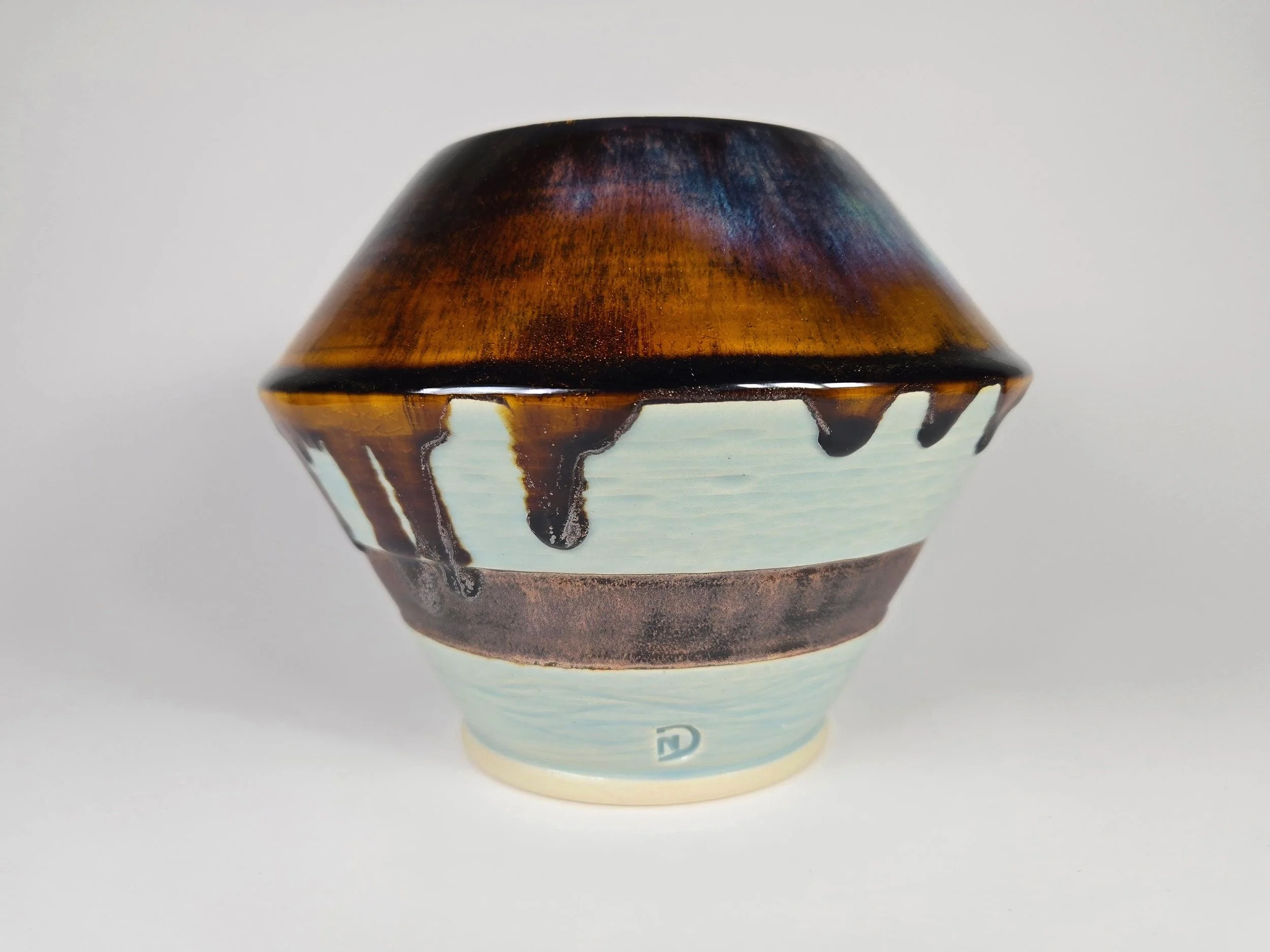 Ceramic bowl with a brown, black, and white glaze design, featuring drip patterns and a small blue logo at the bottom.