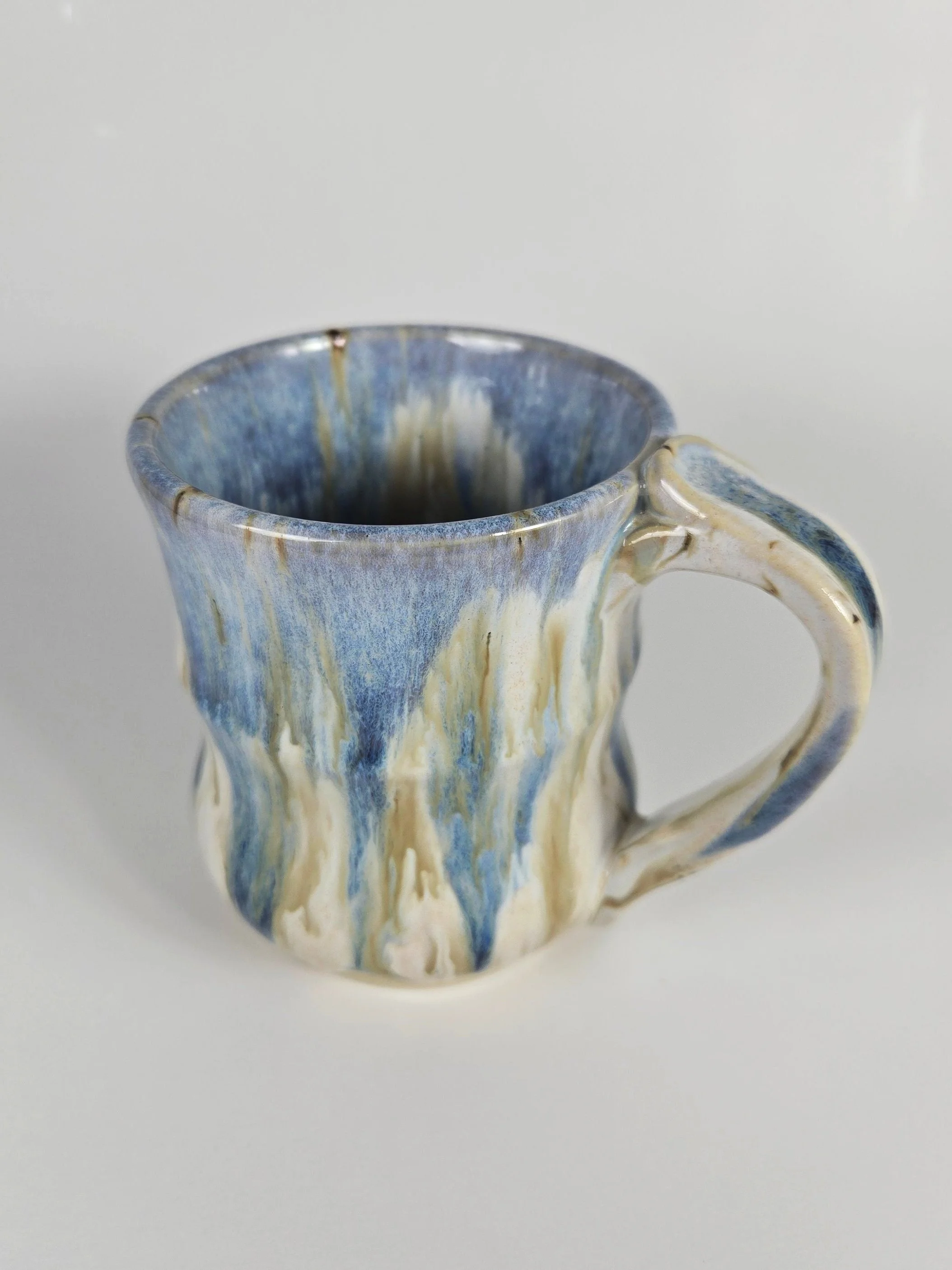 Ceramic mug with blue and white marbled glaze, sitting on a white surface against a plain background.