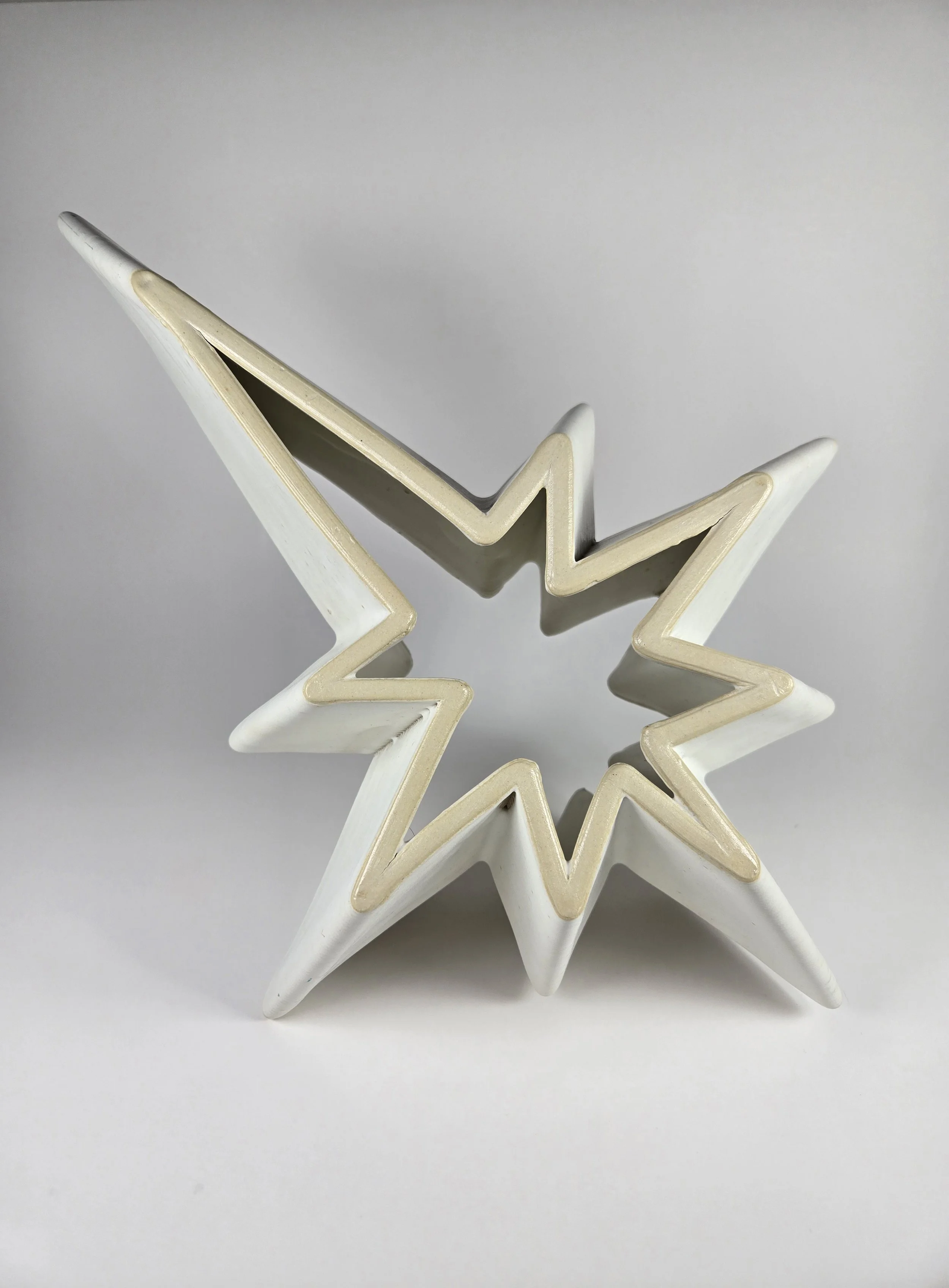 Matte white ceramic star-shaped piece that was ceramic 3D printed, placed on a plain white surface.