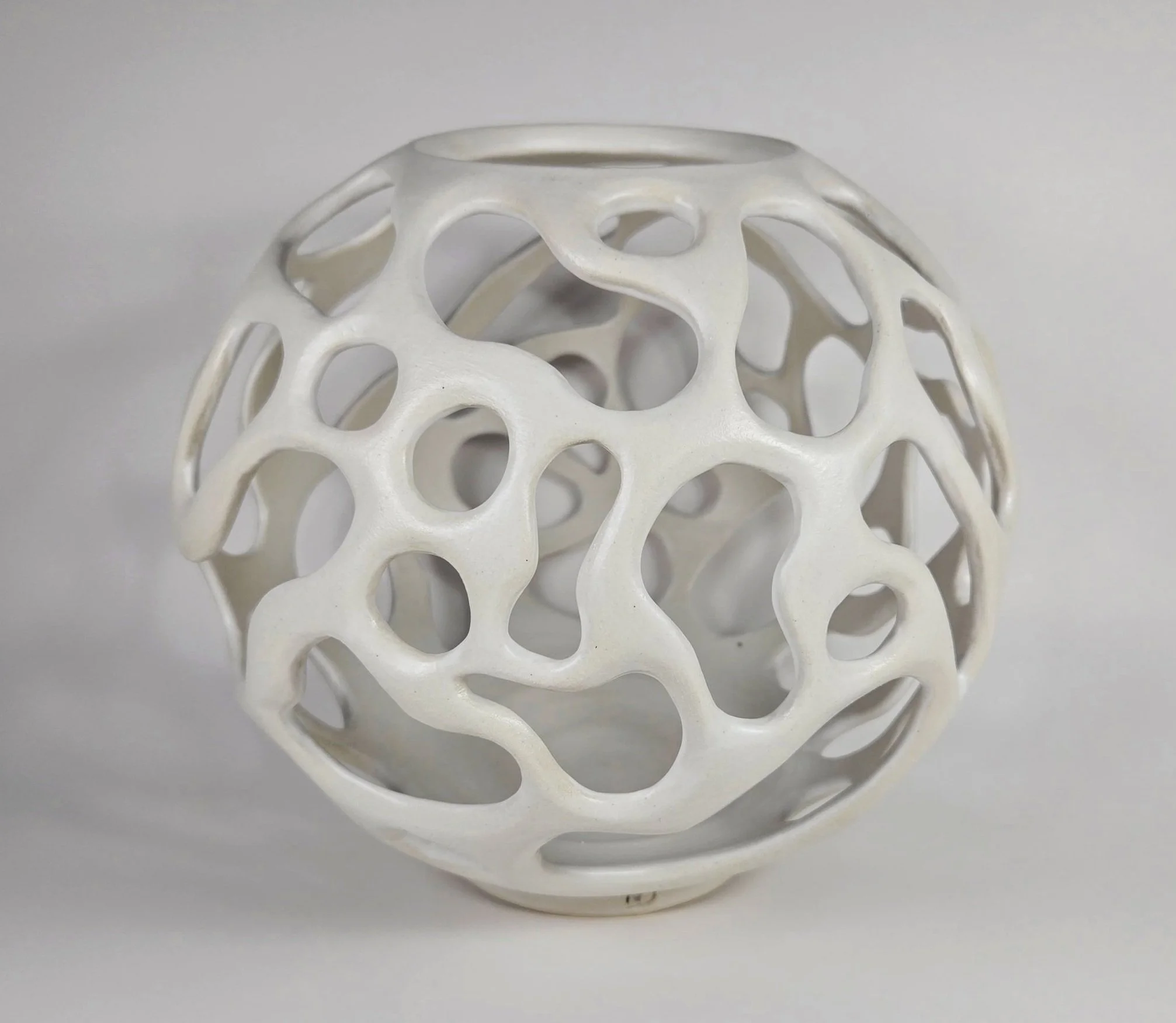 White ceramic decorative sphere with openwork abstract design.