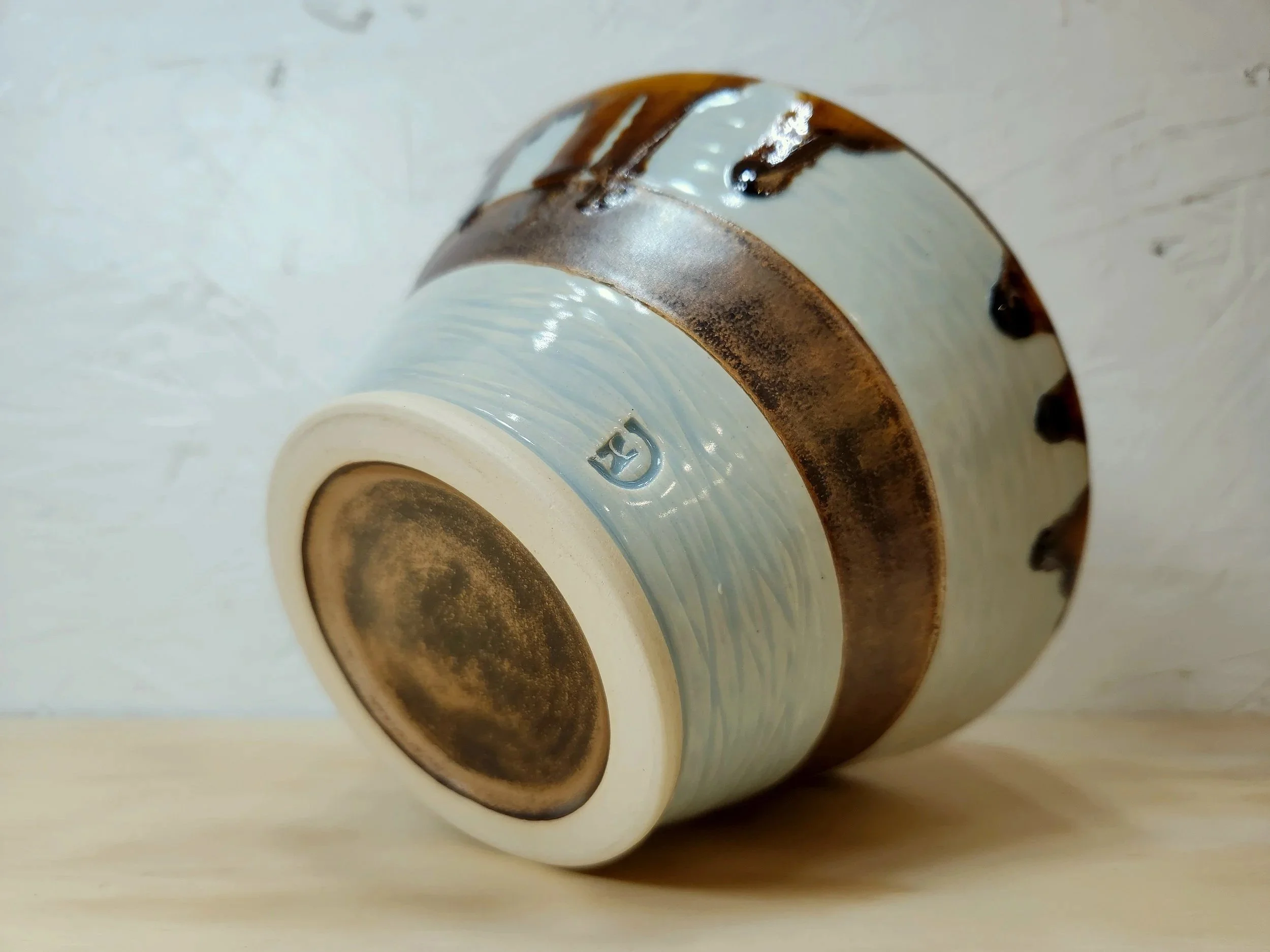 Close-up of tarnished and rusted metallic part with painted surface and a small logo or marking on the edge, lying on a light-colored wooden surface.