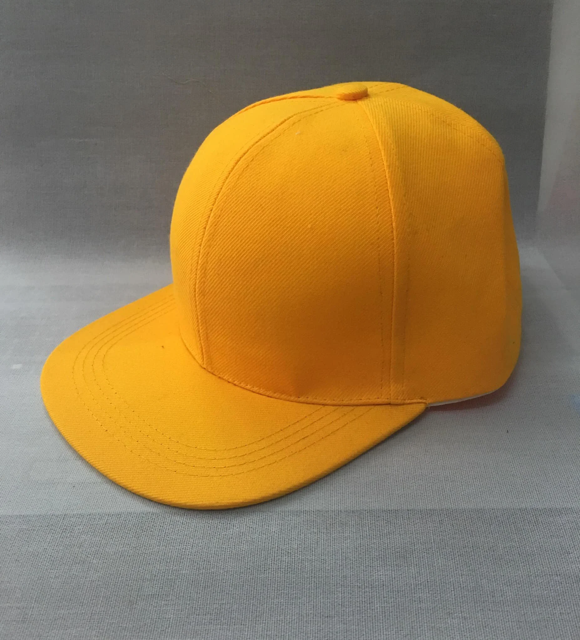 A yellow baseball cap on a light gray surface with a gray background.