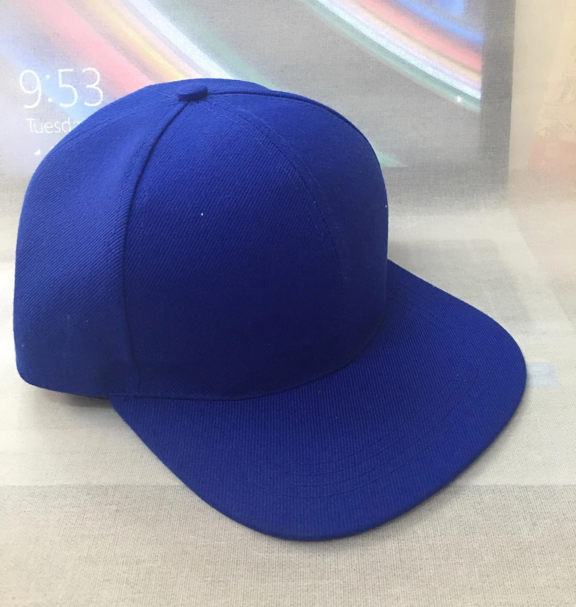 A bright royal blue baseball cap on a table in front of a computer monitor.