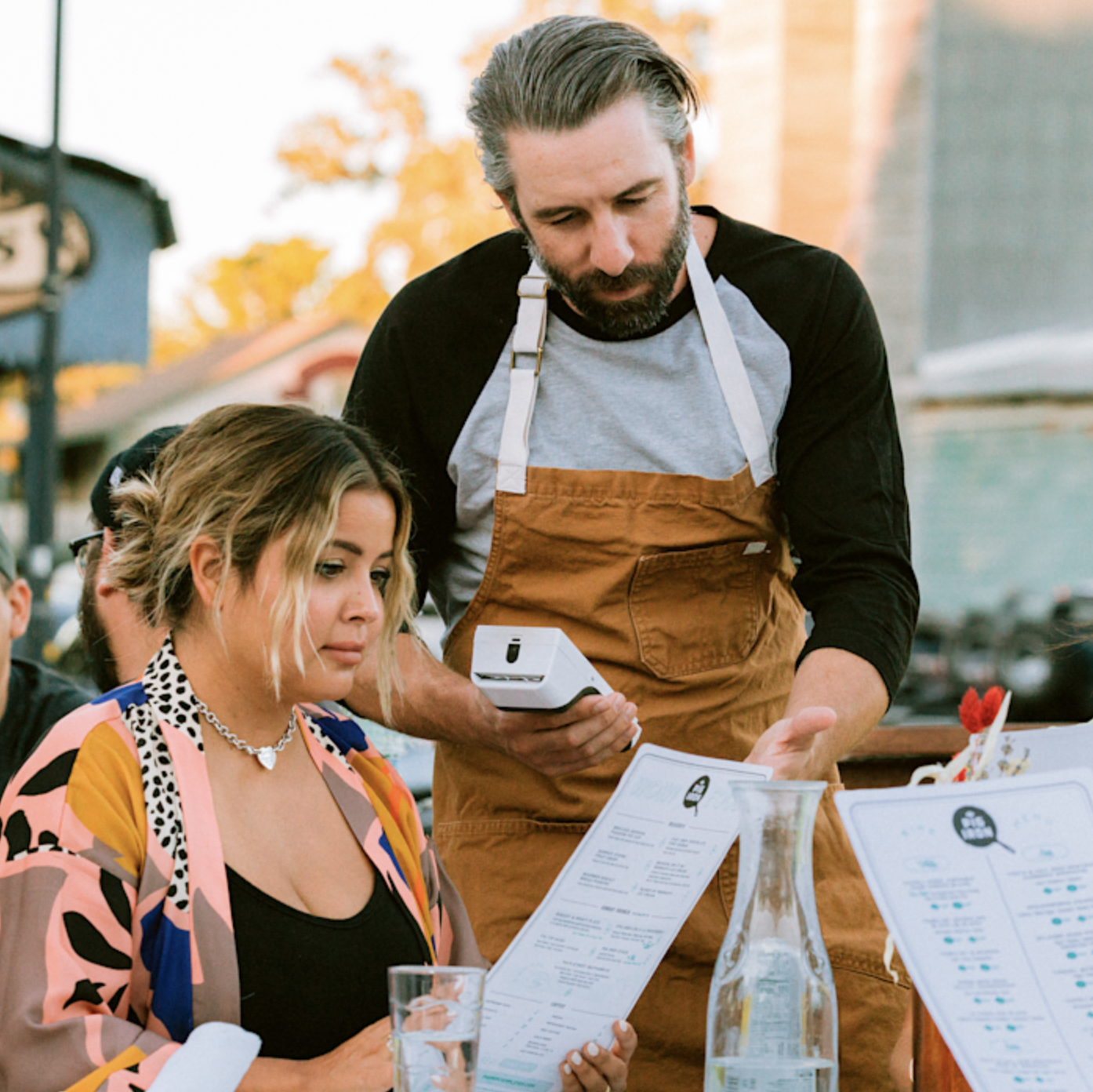 Waiter taking an order from woman at outdoor restaurant table.